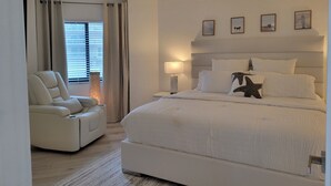 Une chambre à coucher avec un grand lit, une chaise, une table de chevet et une fenêtre avec des rideaux.