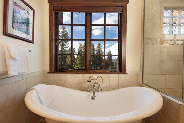 A bathroom with a freestanding bathtub, a window with a view of trees, and a shower area.