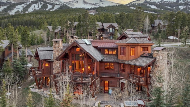 Un grand chalet à étages, doté d’une cheminée en pierre, d’une façade en bois et de nombreuses fenêtres.