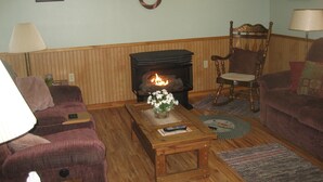 A cozy living room with a fireplace, two armchairs, a coffee table with a vase of flowers, and a 'Welcome' sign above the mantelpiece.