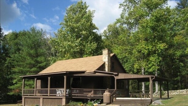 A cabin with a covered porch, a chimney, and a stone fireplace.