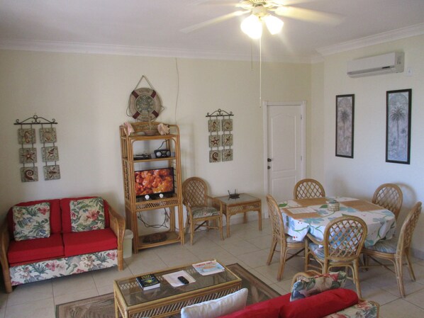 Uma sala de estar com um sofá vermelho, uma mesa de centro de vidro, uma mesa de jantar com cadeiras, um ventilador de teto e decorações nas paredes.