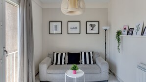 Ein modernes Wohnzimmer mit einem grauen Sofa, schwarz-weißen Kissen, einem kleinen weißen Tisch mit einer Pflanze und einer Hängelampe.