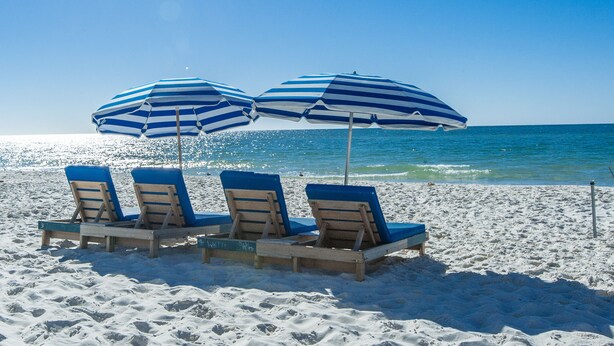 Una playa con tres sombrillas a rayas y sillones de madera.