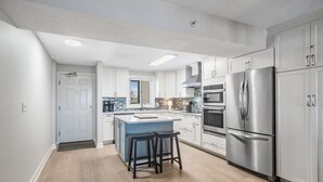 Una cocina moderna con armarios blancos, electrodomésticos de acero inoxidable y una isla central con taburetes.