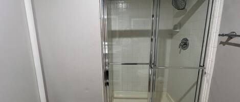 Una ducha con cerramiento de vidrio, piso de baldosas y rociador.
