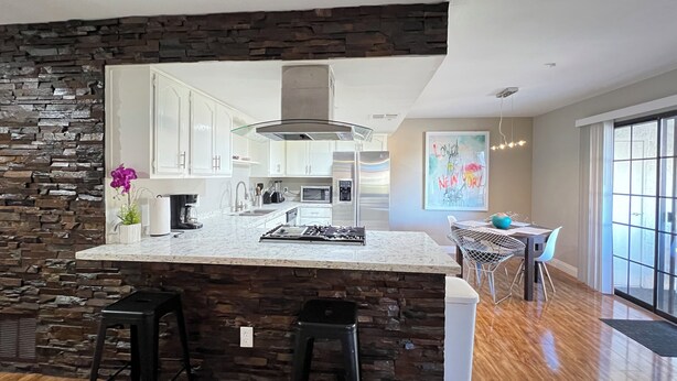 Una cocina moderna con una pared de acento de piedra, una isla central con taburetes de bar y una zona de comedor con mesa y sillas.