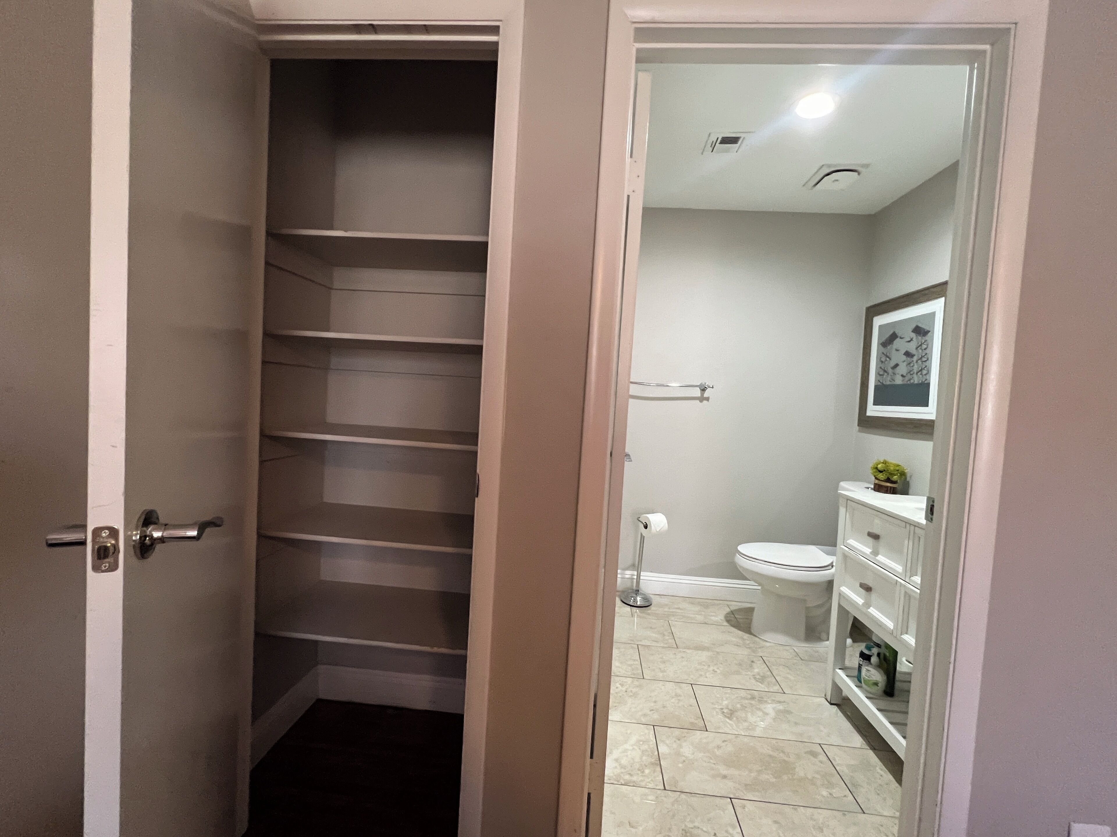 A bathroom with a toilet, sink, and shelves.