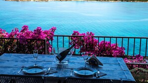 A table set for two with a view of a turquoise sea and mountains in the background.