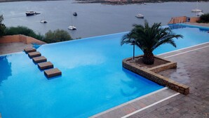 A swimming pool with steps leading down to the water, surrounded by a stone deck.