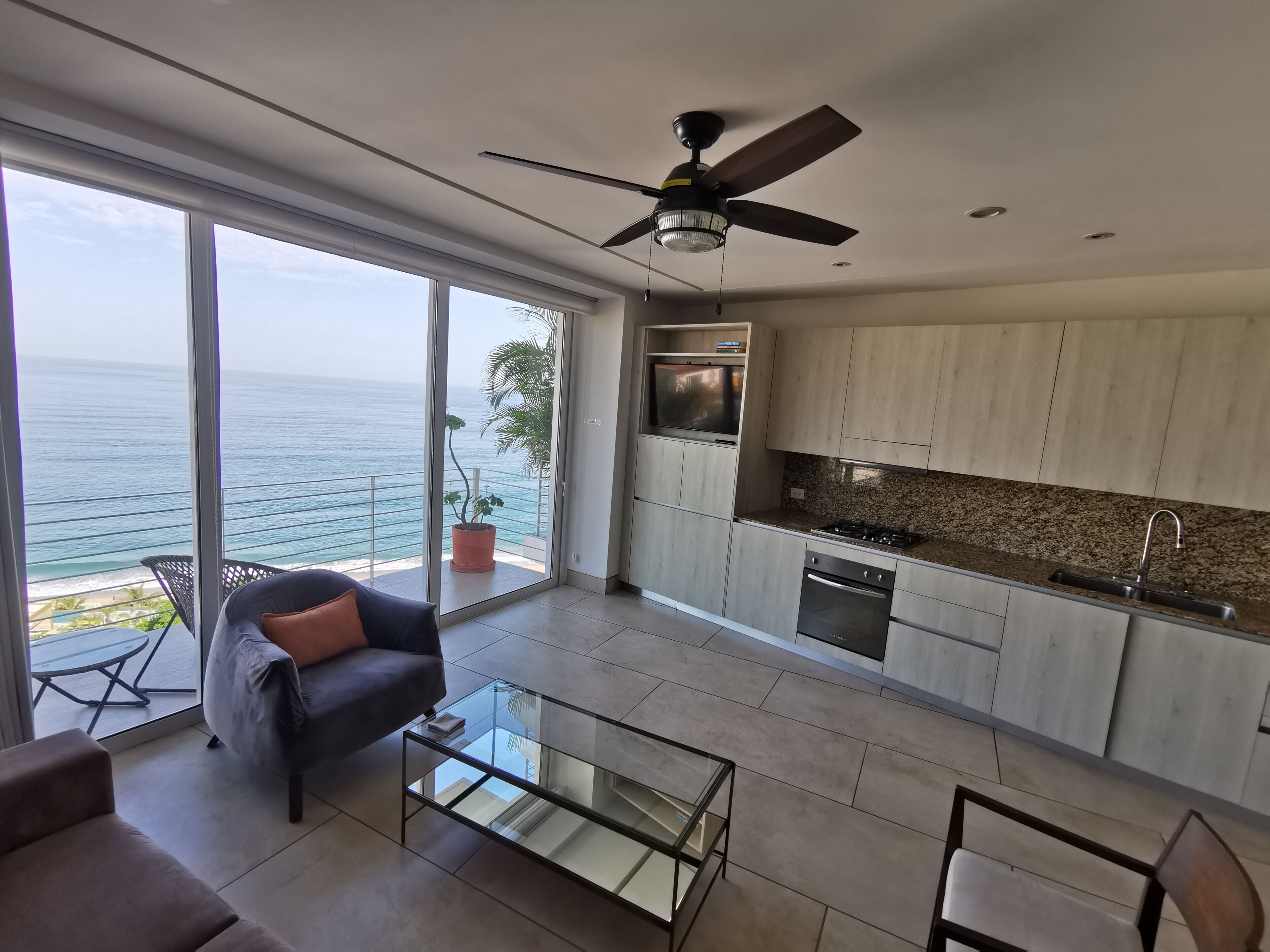 Uma cozinha moderna com vista para o oceano, um ventilador de teto e uma mesa de centro de vidro.