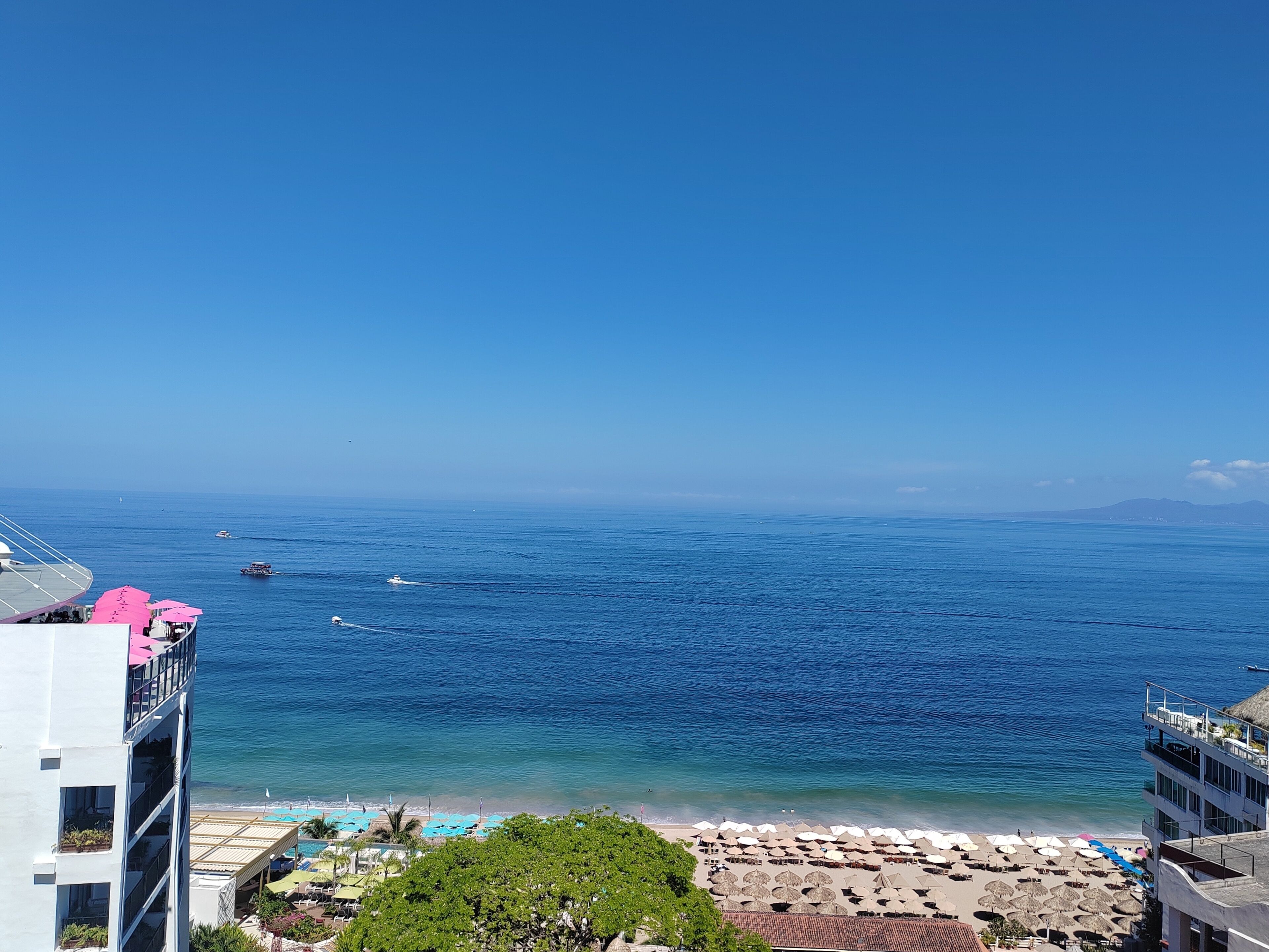 Um hotel à beira-mar com vista para o oceano, área de piscina e guarda-sóis de praia.