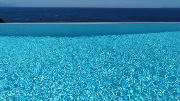 Uma piscina azul e límpida com vista para o oceano e uma praia arenosa.
