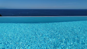 Uma piscina azul e límpida com vista para o oceano e uma praia arenosa.