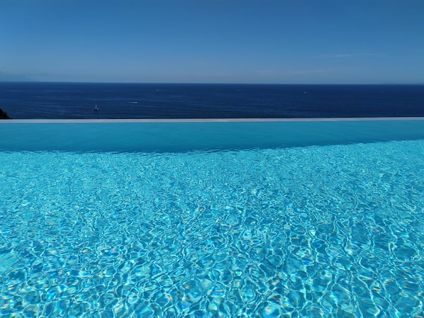 A clear blue pool with a view of the ocean and a sandy beach.