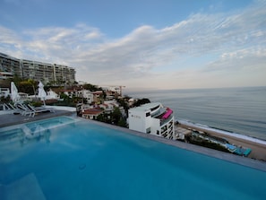 Ein Pool mit Liegestühlen und Blick auf den Ozean, sowie ein Hotelgebäude.