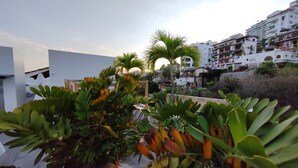 Jardim no terraço com plantas em vasos e vista para uma cidade costeira com edifícios brancos.