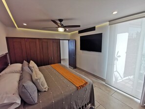 A bedroom with a bed, a ceiling fan, a TV, and a sliding glass door.