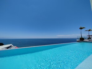 Klar blå himmel, en swimmingpool og havudsigt.