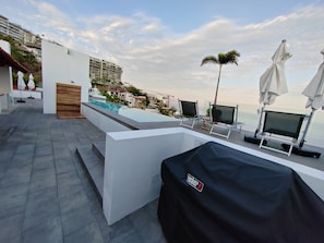 A rooftop pool area with lounge chairs, umbrellas, and a view of the cityscape.