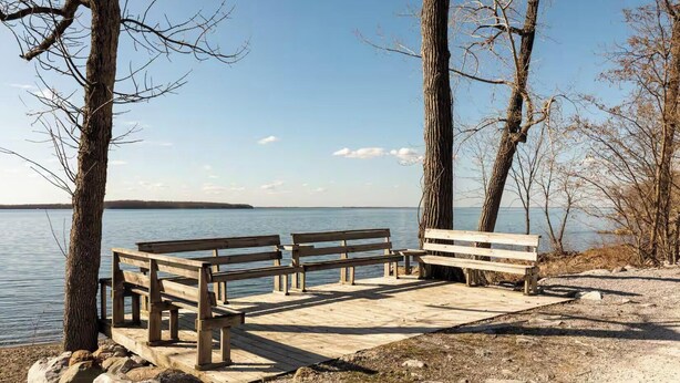 Un banc en bois au bord d’un lac paisible, sous un ciel dégagé.