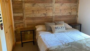 Une chambre à coucher avec une tête de lit en bois, un lit recouvert d’une couette blanche, deux tables de chevet et un oreiller orné du mot « RELAX ».