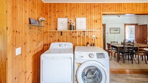 A laundry area with a washer and dryer, wooden walls, a dining area with a table and chairs, and a kitchen visible through an open door. - Family Fun & Sun in Bolton - walking distance to town, beaches, & lake (Bolton)
