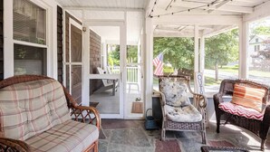 A covered porch with wicker furniture, a flag, and a view of the outdoors. - Family Fun & Sun in Bolton - walking distance to town, beaches, & lake (Bolton)