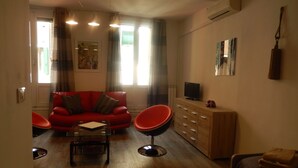 A living room with a red sofa, a wooden cabinet, a television, and a red chair.
