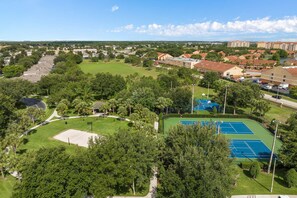 An aerial view of a residential area with a tennis court, surrounded by trees and houses.