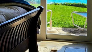 A room with a bed, a chair, and a view of the ocean through a glass door.