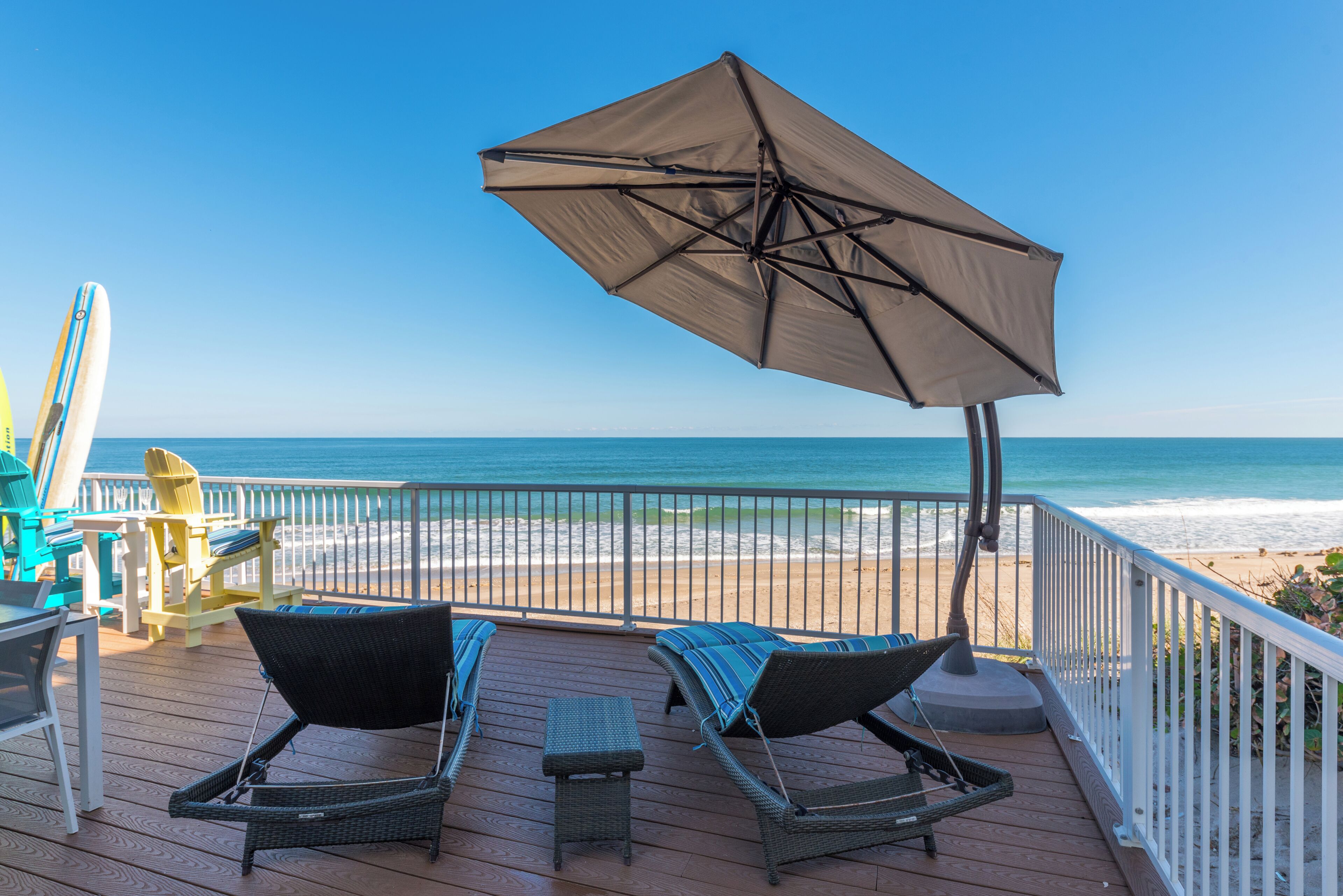 A deck with two lounge chairs and an umbrella, overlooking a beach.