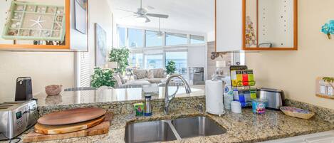 A kitchen with granite countertops, a built-in sink, and a dining area with a view of the ocean.