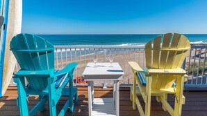 Una terraza con dos sillas Adirondack y una mesita con dos copas de vino, con vista a la playa.