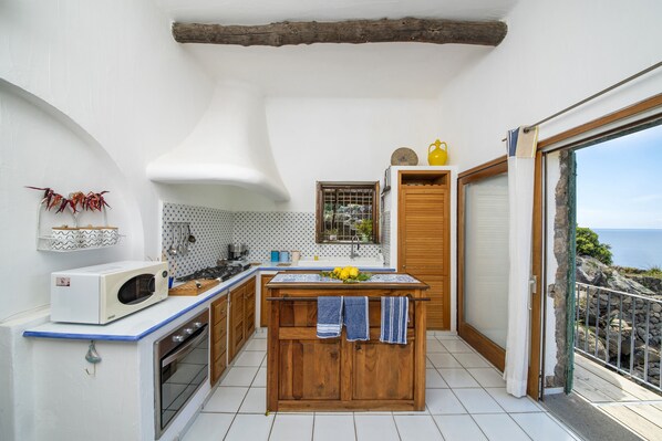Cocina compacta con una isla central, microondas y vistas al mar a través de una puerta corredera.