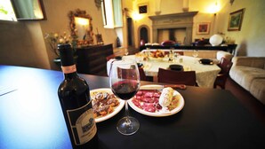 A dining table with a bottle of wine, a glass of red wine, and plates of food in a warmly lit room with arched ceilings and a fireplace. - Luxury Renaissance Palace (Firenze)