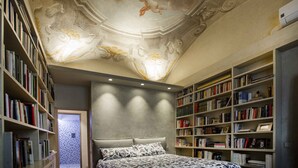 A bedroom with a large bed, bookshelves, and a decorative ceiling. - Luxury Renaissance Palace (Firenze)