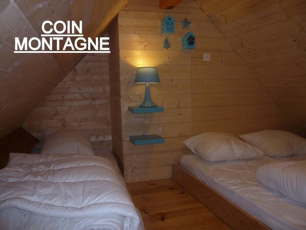 A cozy attic bedroom with two beds, a lamp, and wooden walls.
