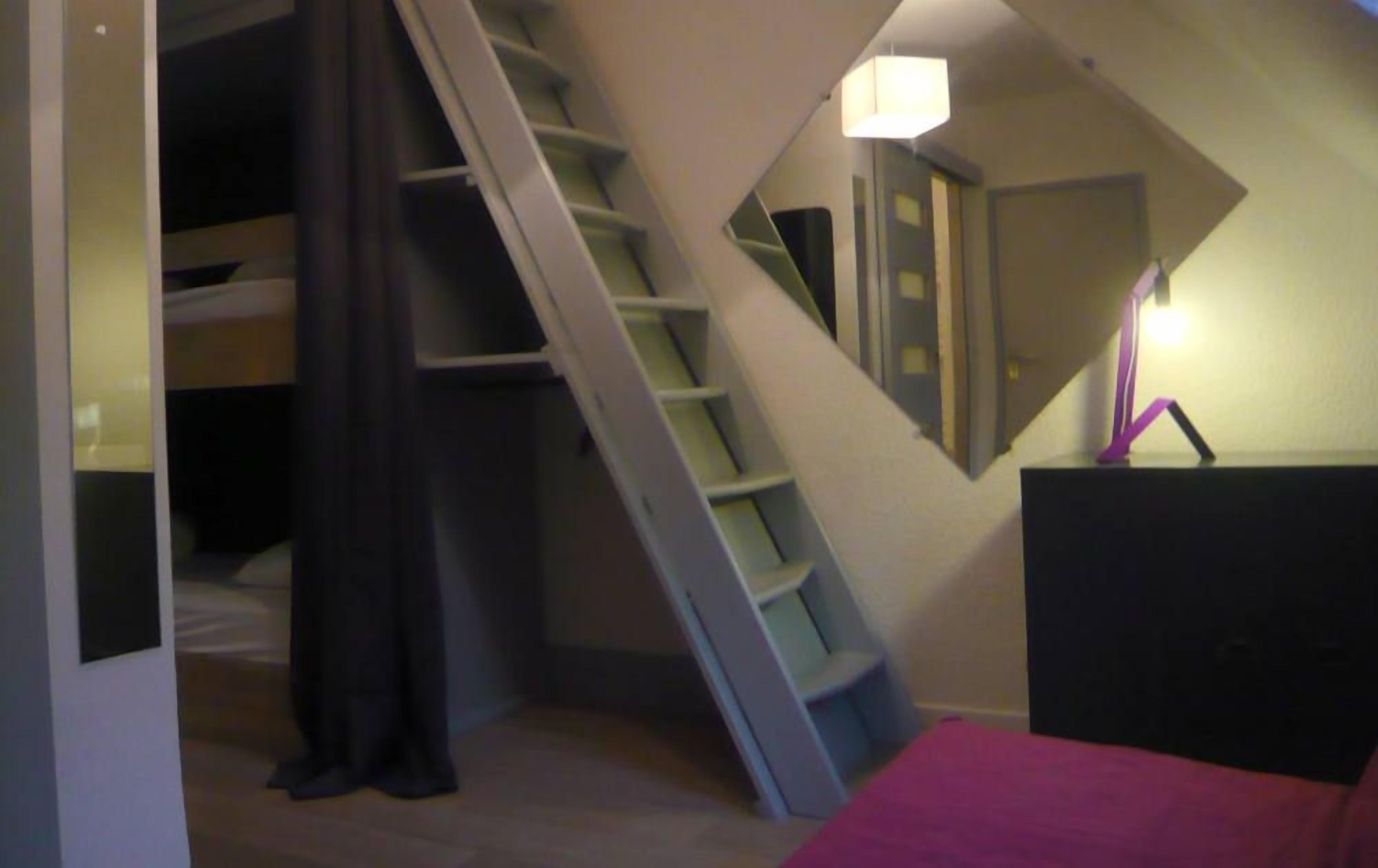 Una habitación con literas, una escalera y un escritorio con lámpara.