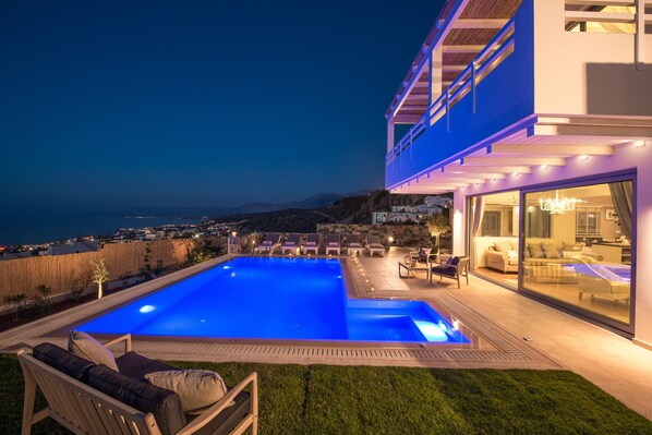 A modern house with a swimming pool, outdoor seating, and a view of the ocean.