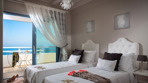 A hotel room with two beds, a balcony with a view of the sea, and a dining area with a table and chairs.