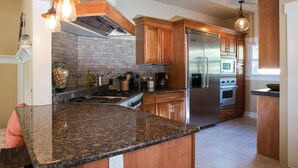 A modern kitchen with granite countertops, stainless steel appliances, wooden cabinets, and pendant lighting.