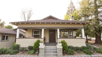A two-story house with a front porch, a chimney, and a small front yard with potted plants.
