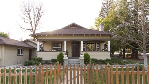 A two-story house with a front porch, a picket fence, and a chimney.