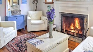 A cozy living room with a fireplace, white sofas, a blue cabinet, and a vase with purple flowers. - Wonderful location, walk to beach, private yard, Voted #1 in town by AB&B (old saybrook)