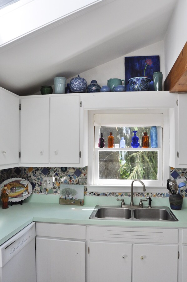 Una cocina con armarios blancos, una ventana con botellas en el alféizar y un salpicadero colorido.