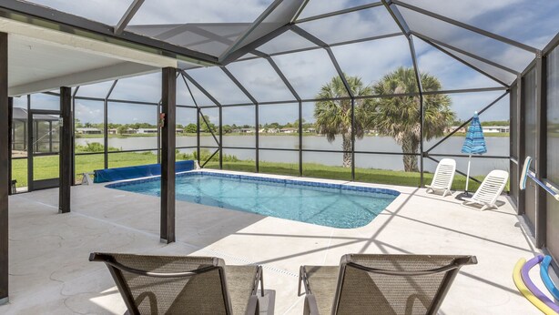 Une piscine extérieure couverte, dotée de chaises longues et offrant une vue sur un lac et des palmiers.
