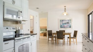 Une cuisine moderne avec des meubles blancs, un coin repas avec des chaises en bois et un tableau au mur.