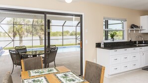 Une cuisine moderne avec des meubles blancs, un plan de travail noir et une fenêtre donnant sur une piscine.