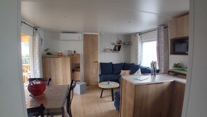 A compact living space with a kitchenette, a dining area, and a seating area with a sofa and a small round table. - Spacious, comfortable mobile home for 6/8 people (40m2) (Les Mathes)